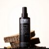 STMNT Grooming Spray fles met hout en koffiebonen op achtergrond.
