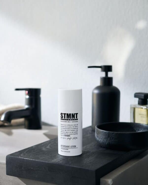 STMNT aftershave lotion op zwart houten plank in badkamer.